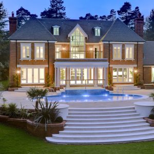 Rear view of a property with a pool. The property is lit up and showcases the stone work.